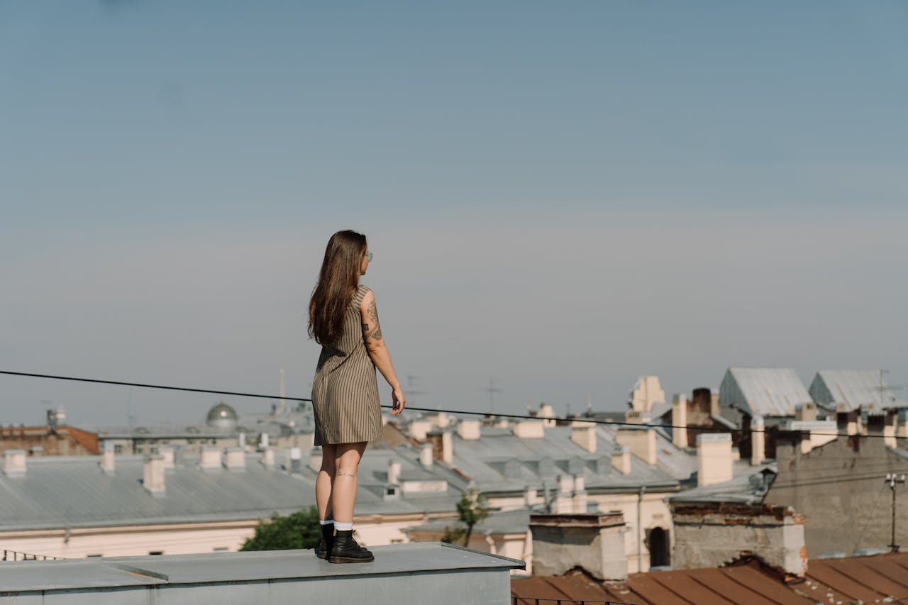 services-03 A woman stands on a rooftop, gazing over an urban cityscape under a clear blue sky.