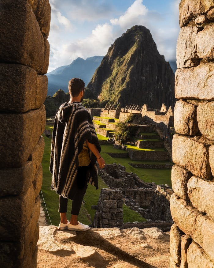 services-04 A man in traditional clothing overlooks the ancient ruins of Machu Picchu during daytime.